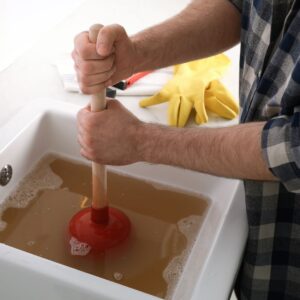 a person using a plunger on a backed up sink