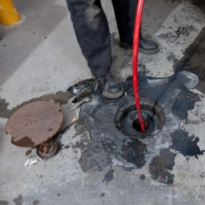 a worker putting a hydro-jet hose down a drain